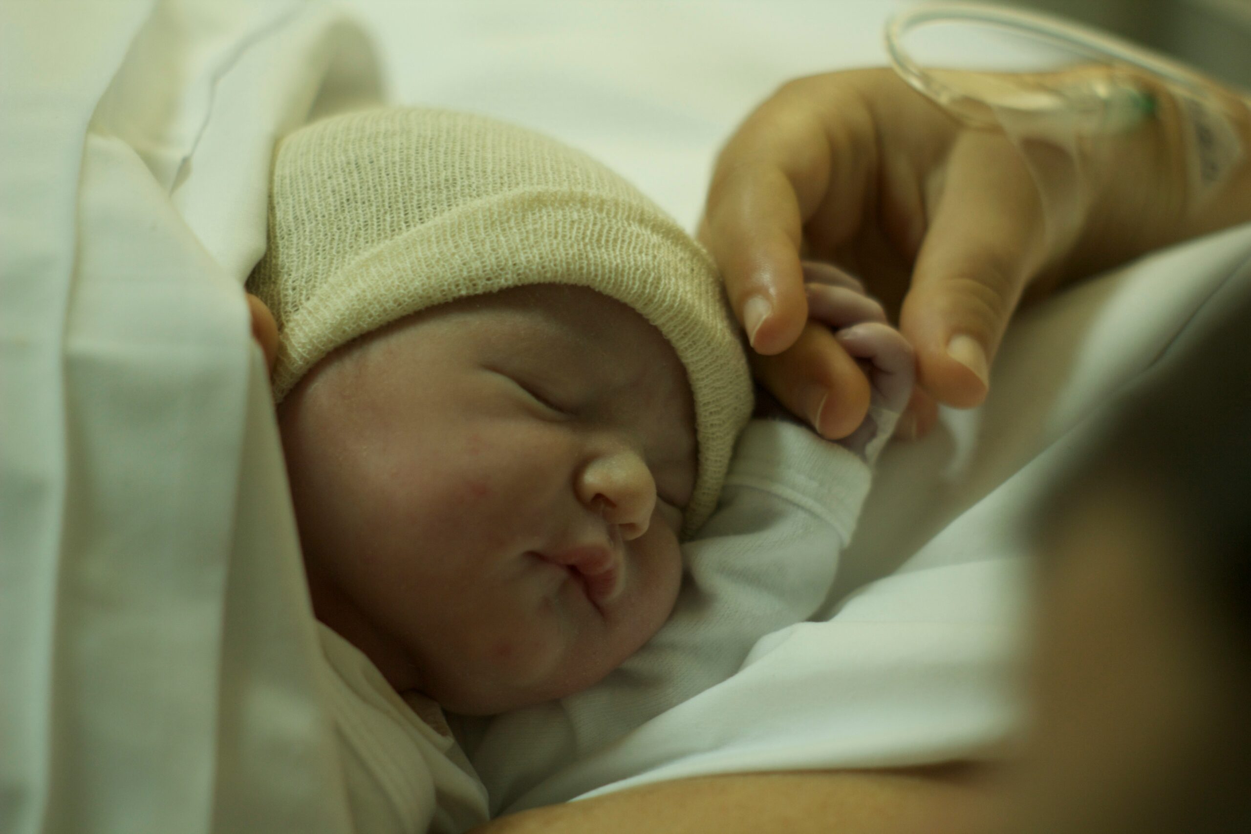 A newborn baby in hospital, being touched by their mother's hand.